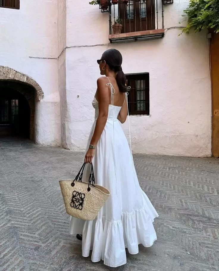 How to Style Old Money for Summer | Elegant woman in a white summer dress carrying a Loewe basket bag in a sunlit Spanish courtyard – old money summer aesthetic. | elle blonde luxury lifestyle destination blog