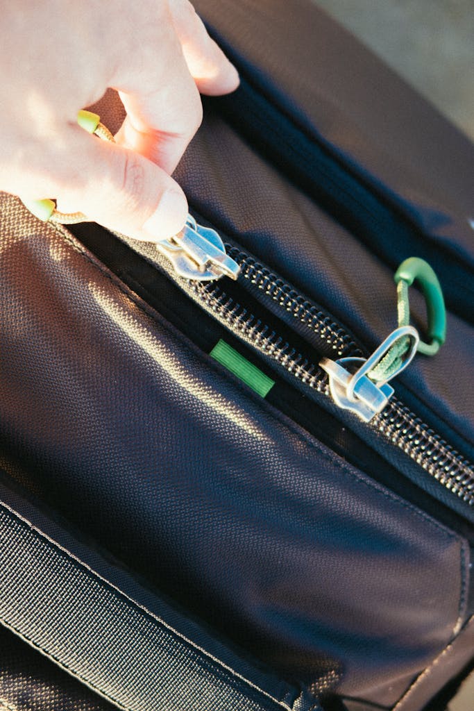 Luxury Hiking Holiday: What to Pack for an Inn-to-Inn Trip 3 A close-up image showing a hand unzipping a stylish black leather bag in daylight.