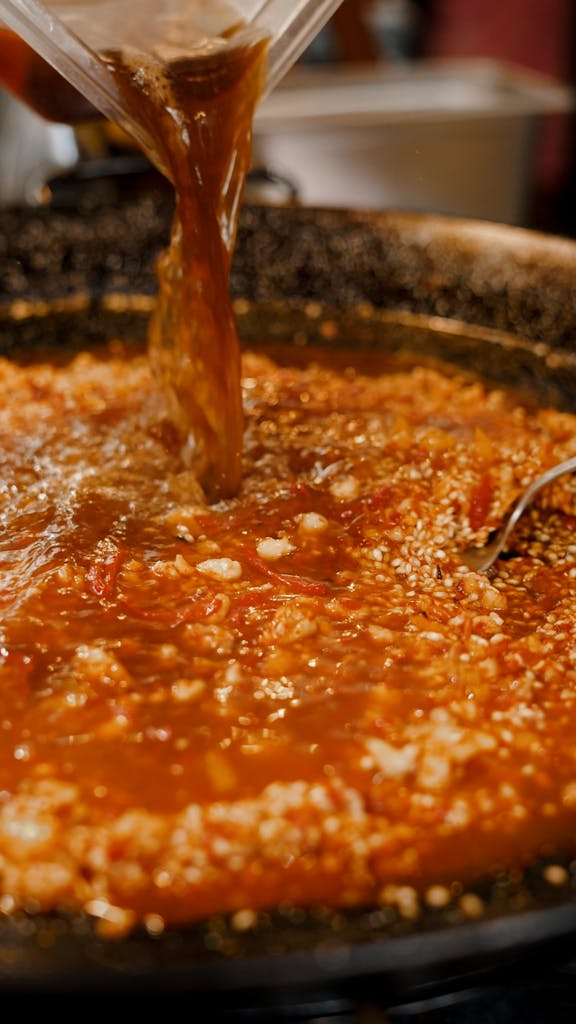 A close-up view of broth being added to a traditional Spanish paella in a pan.