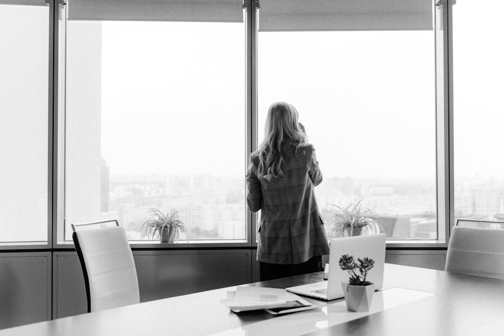 A female executive gazes out the window in a modern office setting, in grayscale photography.