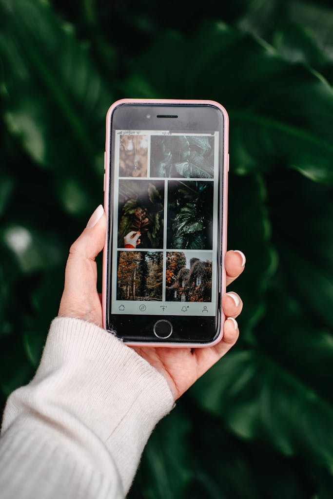 How to Build an Online Business That Funds Your Freedom 3 A hand holding a smartphone displaying nature images, set against lush green foliage.