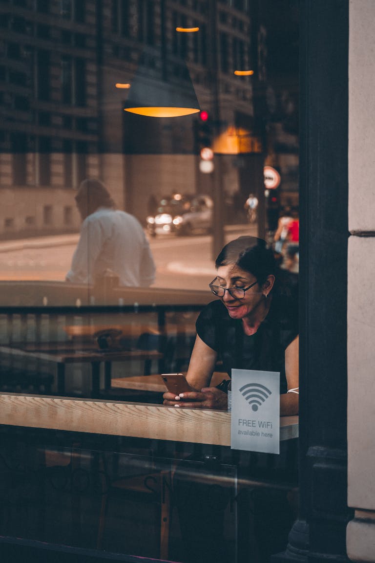 A woman using her smartphone at a cafe window in London, reflecting urban lifestyle.