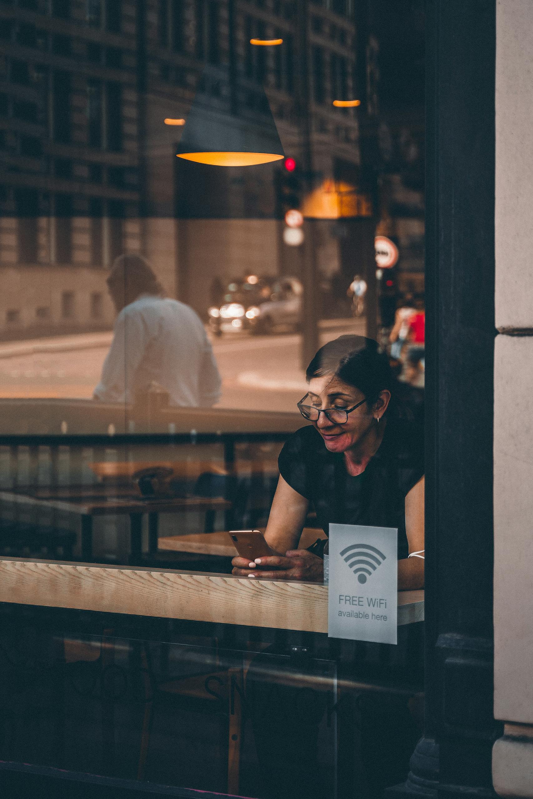A woman using her smartphone at a cafe window in London, reflecting urban lifestyle.