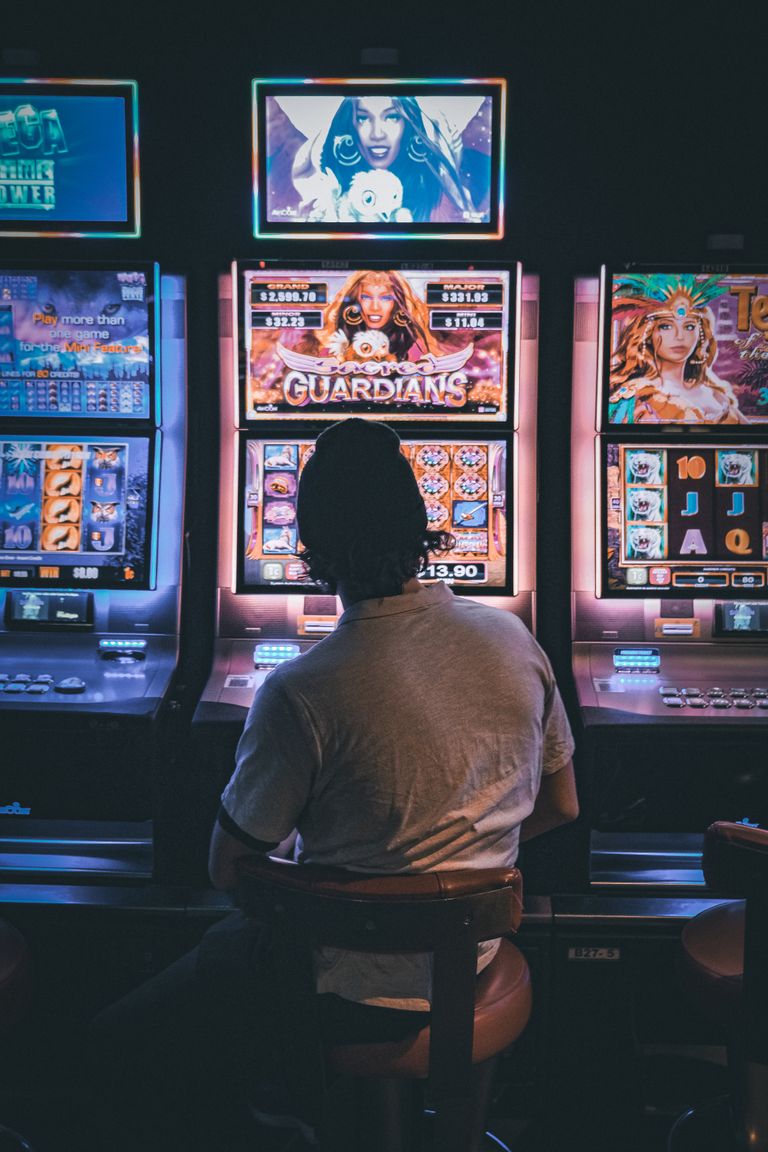 Adult male seated in a dimly lit casino engaging with vibrant slot machines at night. Swedish license