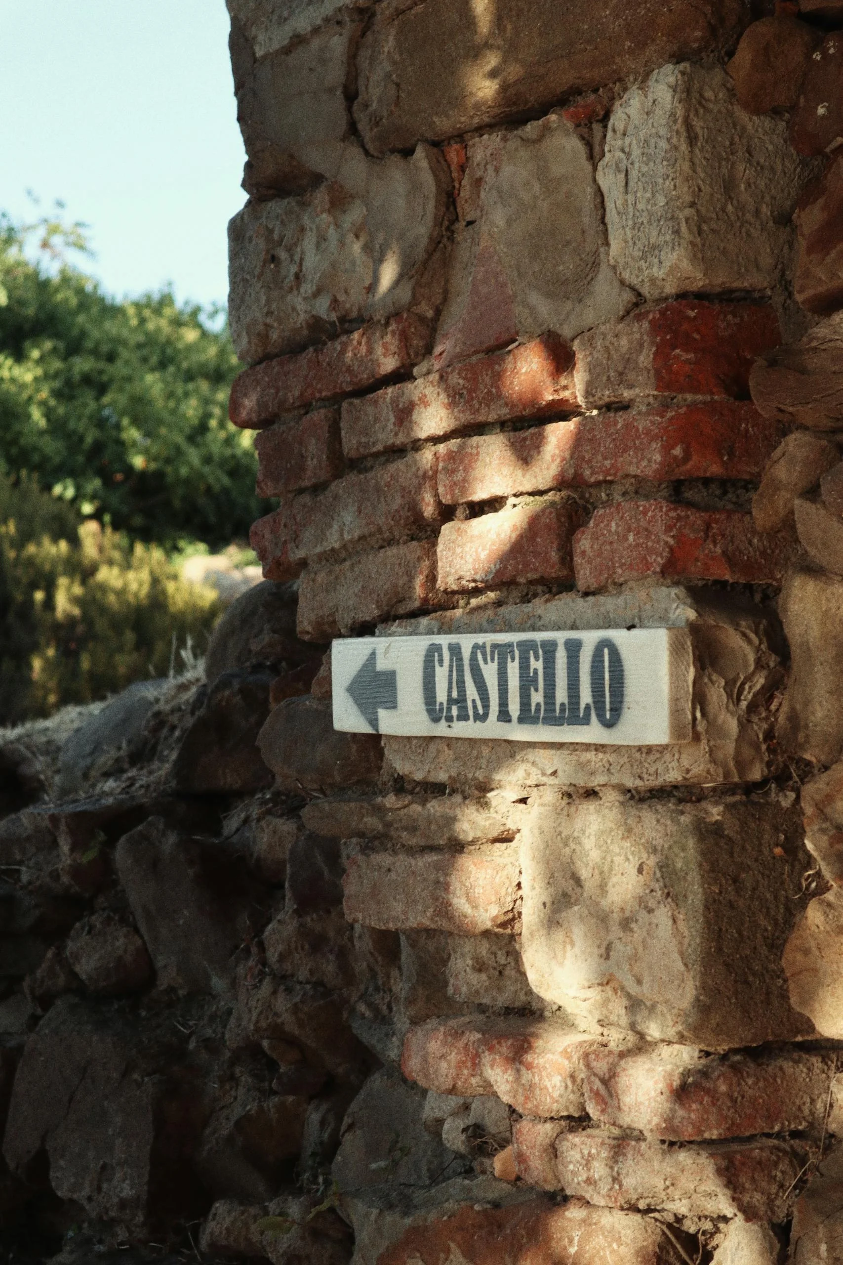 A directional sign pointing to a castello on a historic brick wall in sunlight.