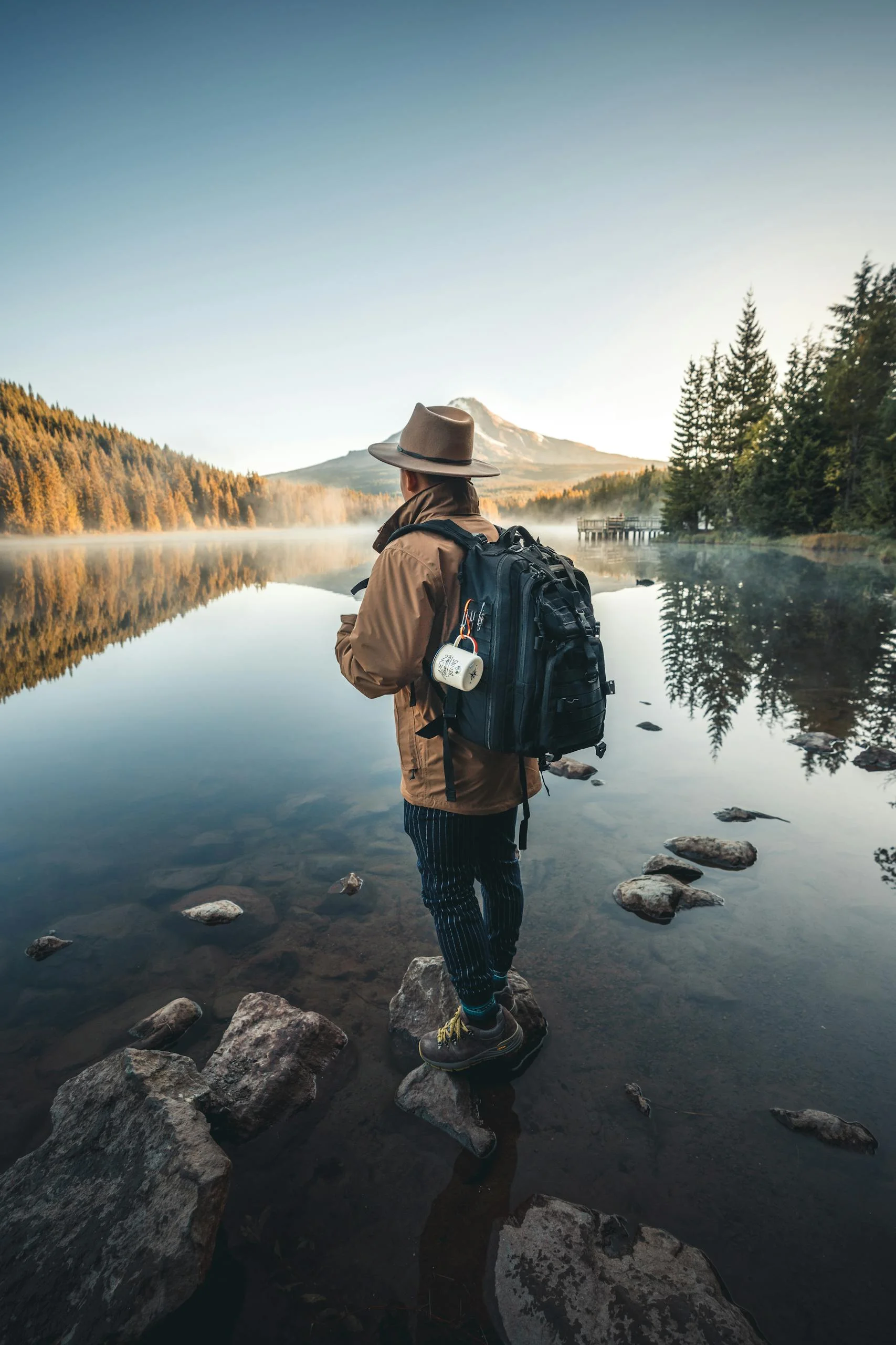 A hiker with a backpack stands by a tranquil mountain lake, capturing the essence of adventure and serenity. | Luxury hiking - elle blonde luxury travel blog for women who monetise