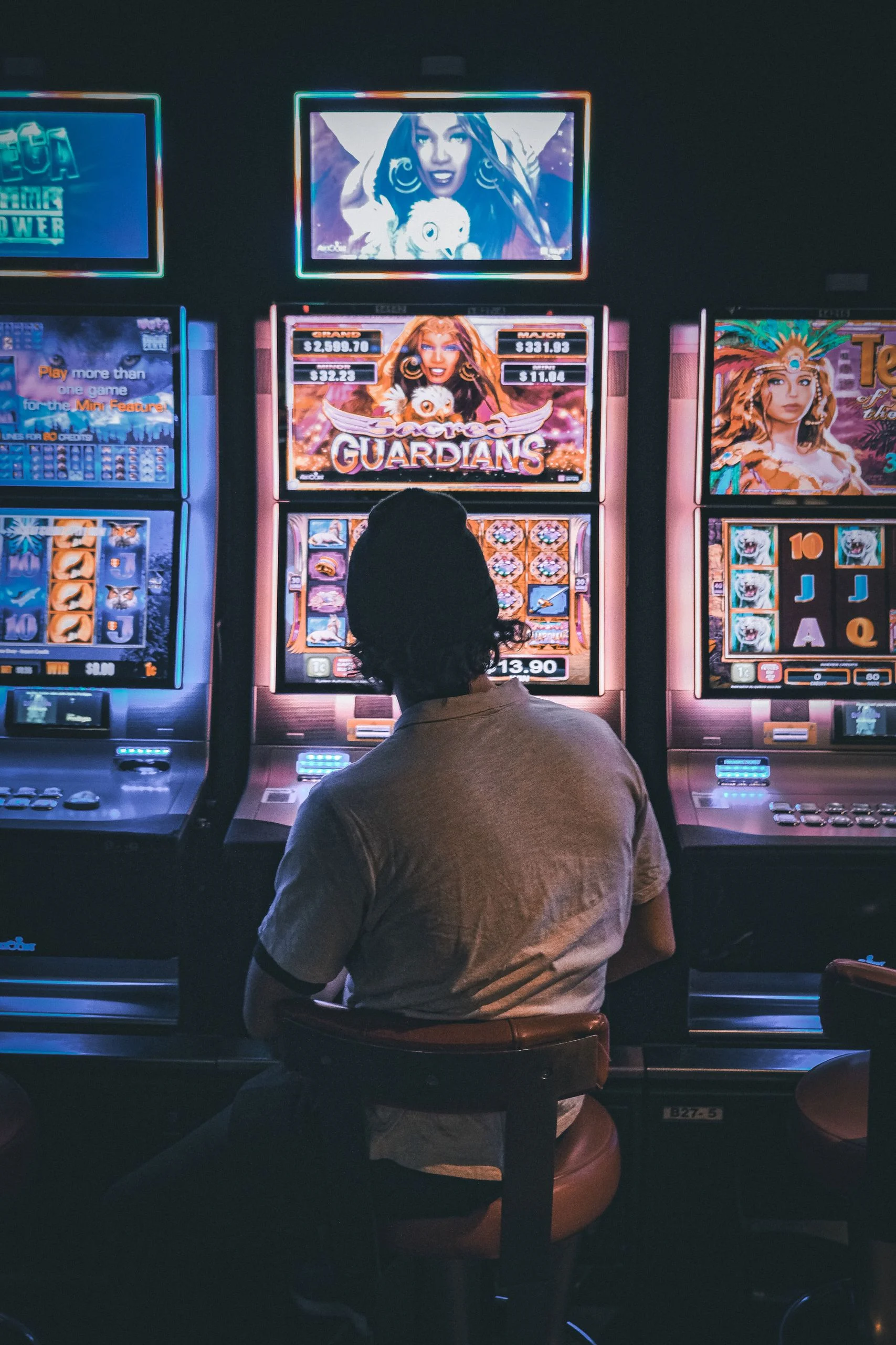 Adult male seated in a dimly lit casino engaging with vibrant slot machines at night. Swedish license