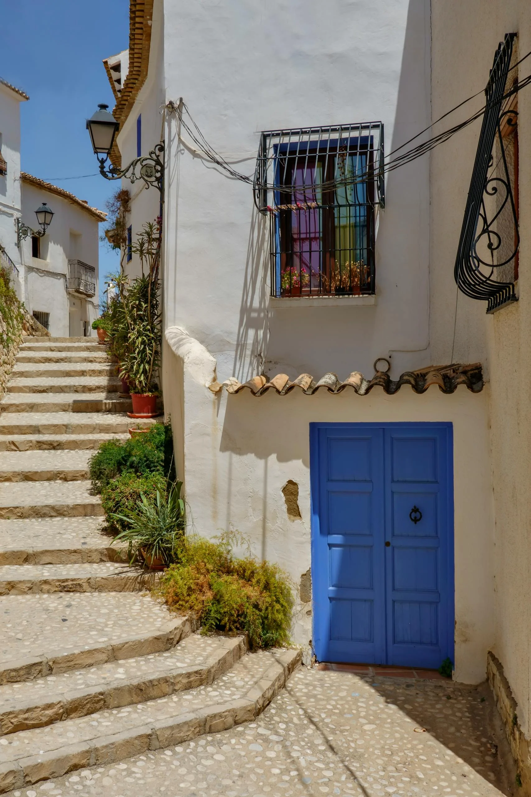 Charming street scene in Alicante, Spain with a vibrant blue door and cobbled steps.