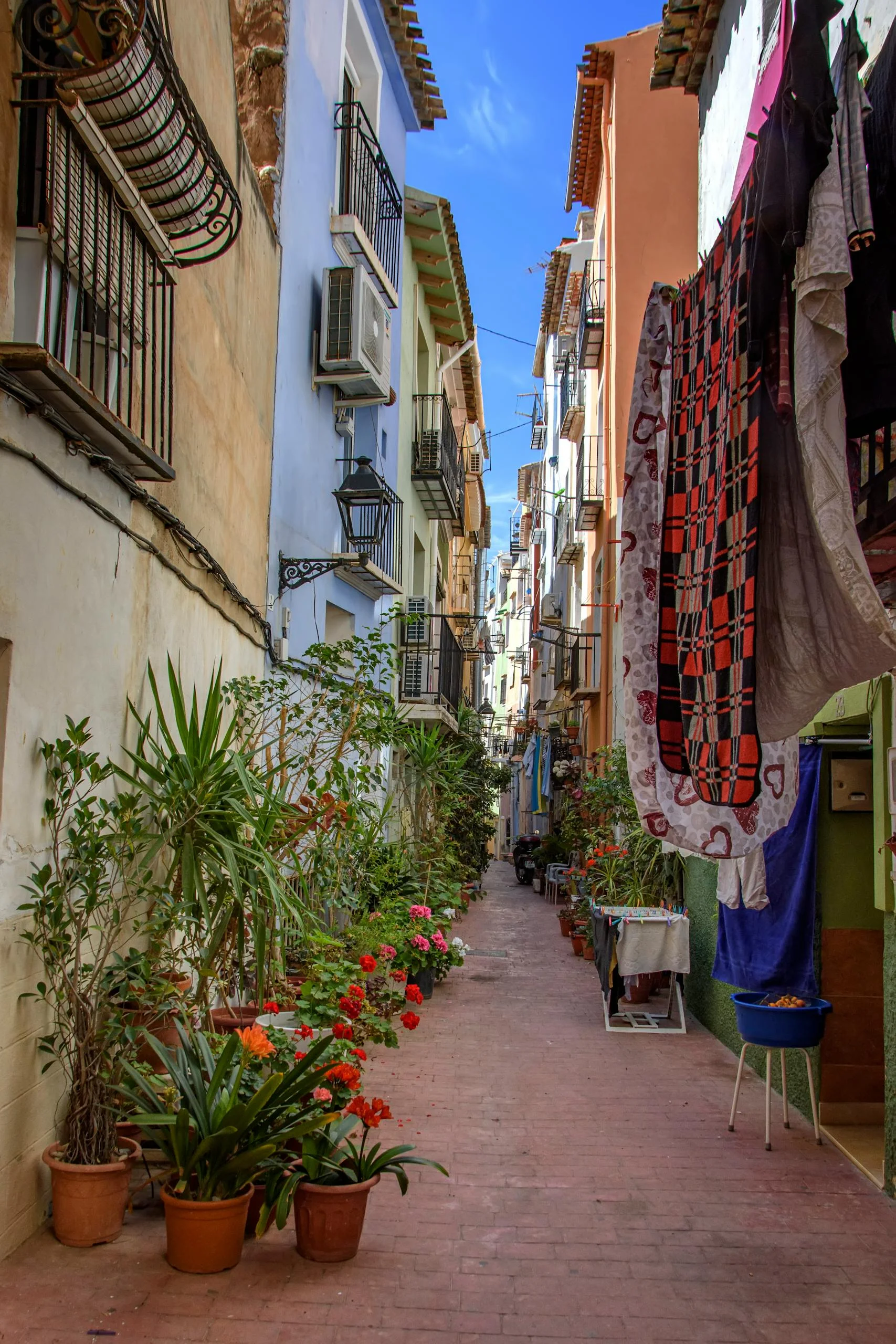 Colorful narrow street with potted plants and hanging laundry in Villajoyosa, Spain.