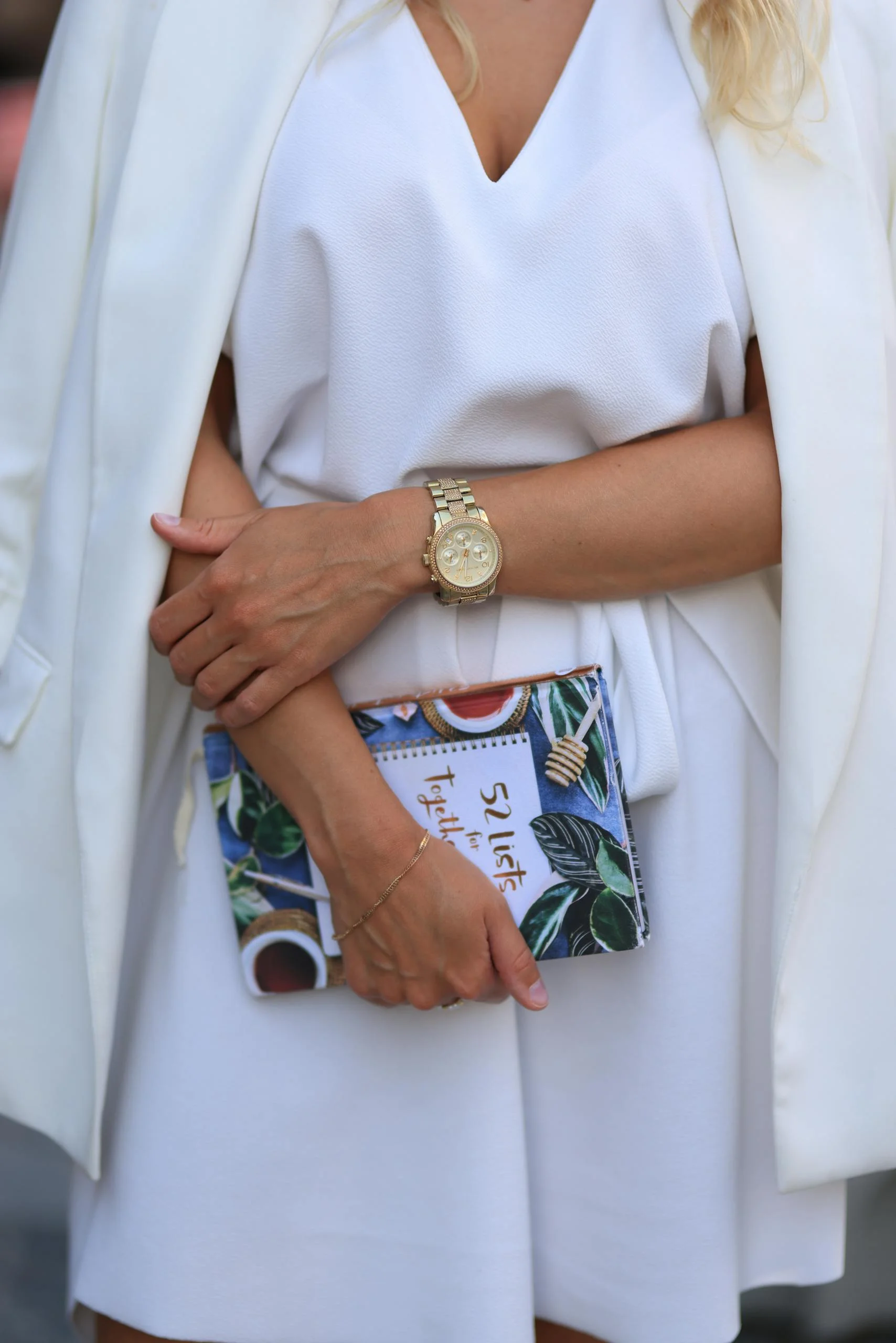 Fashionable woman in white holding a decorated book with stylish watch.