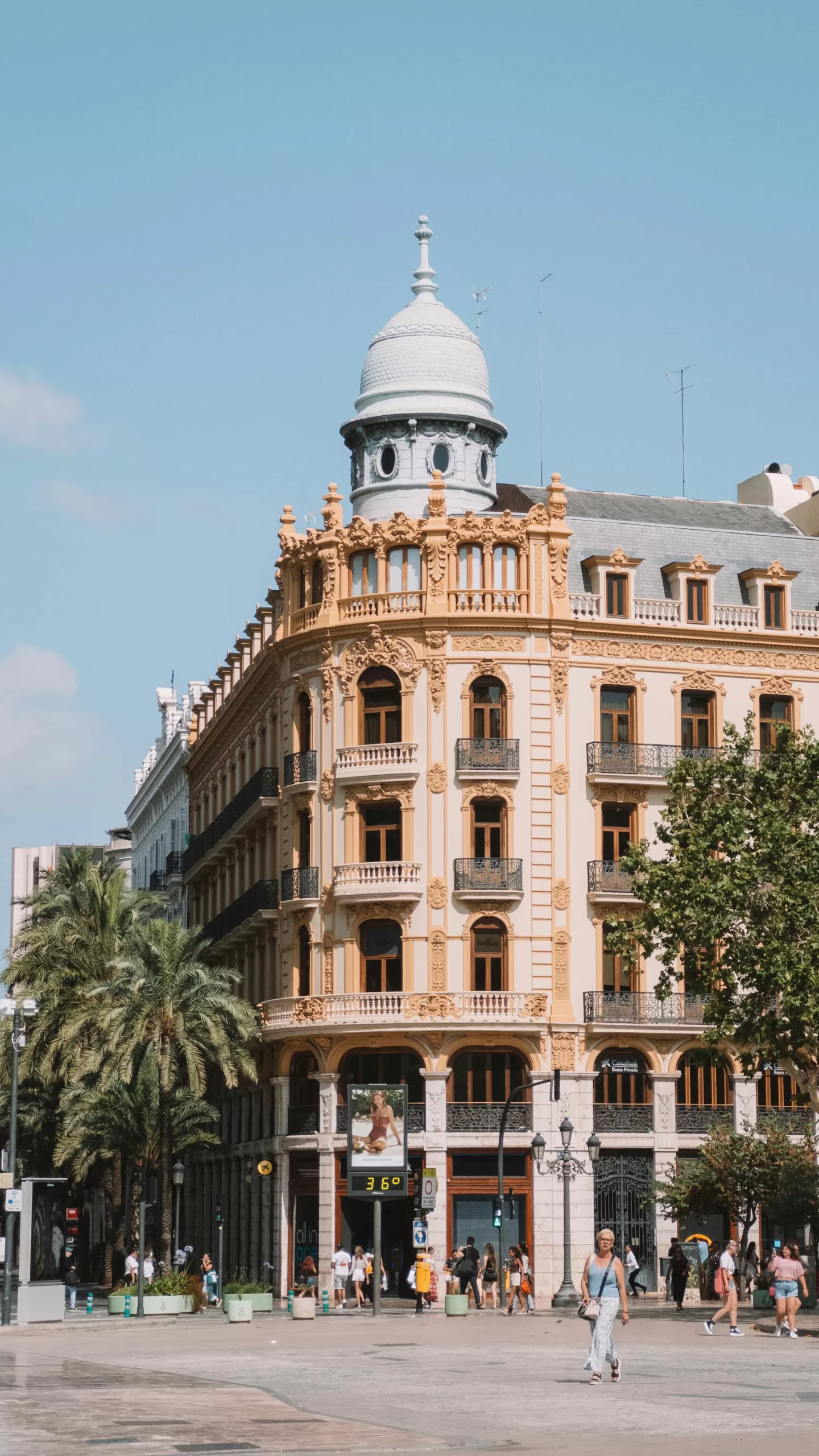 Grand baroque-style building in Valencia’s city centre on a sunny day, surrounded by palm trees and local pedestrians – a vibrant scene in one of Spain’s cultural gems. | Travel Tips | elle blonde Luxury Lifestyle Destination Blog