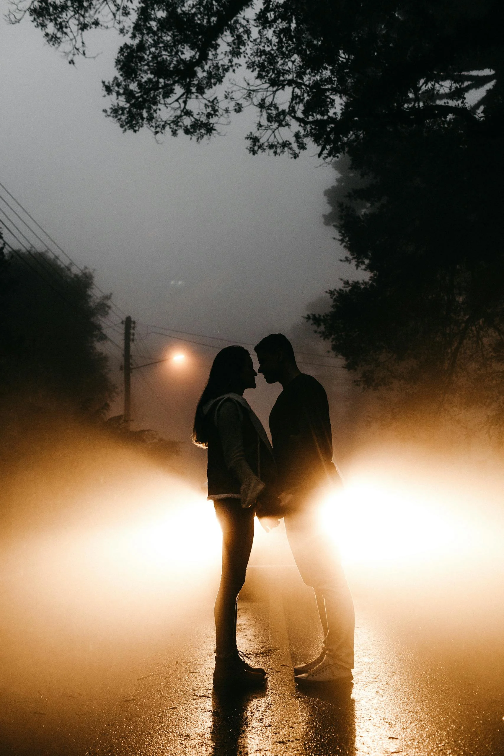 Silhouetted couple standing in front of car headlights on a foggy night, embracing romance. manifest love after heartbreak