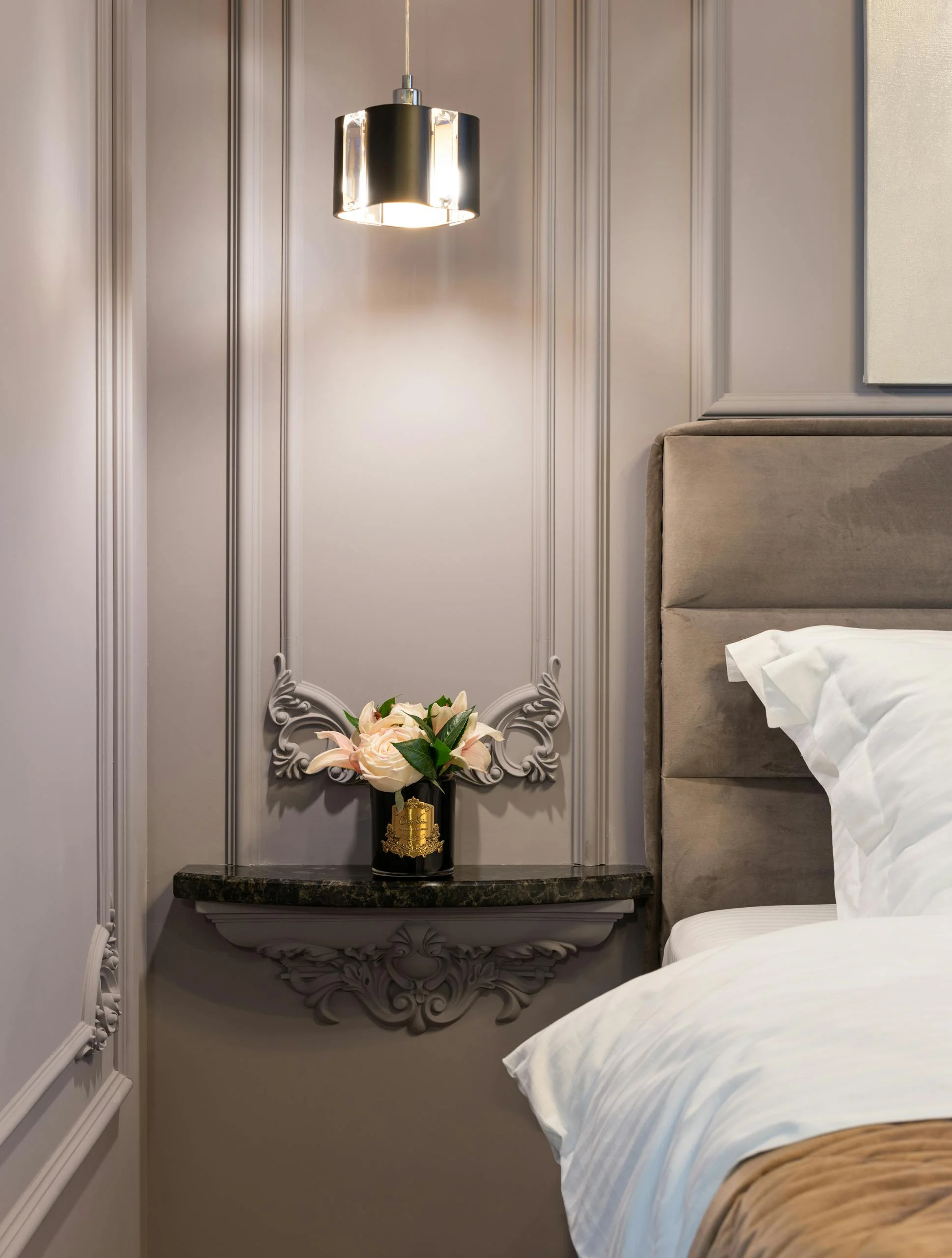 Soft bed near vase with blossoming flowers on decorative shelf under glowing light at home