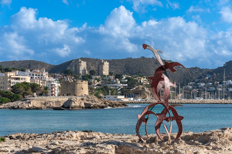 Artistic sculpture on the rocky shore of Moraira with coastal scenery.
