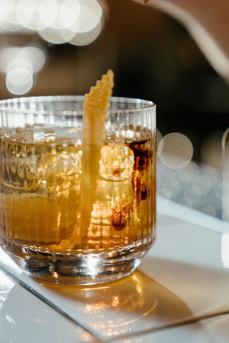 Close-up of a whiskey glass with citrus garnish on a bar table, perfect for cocktail and beverage themes.