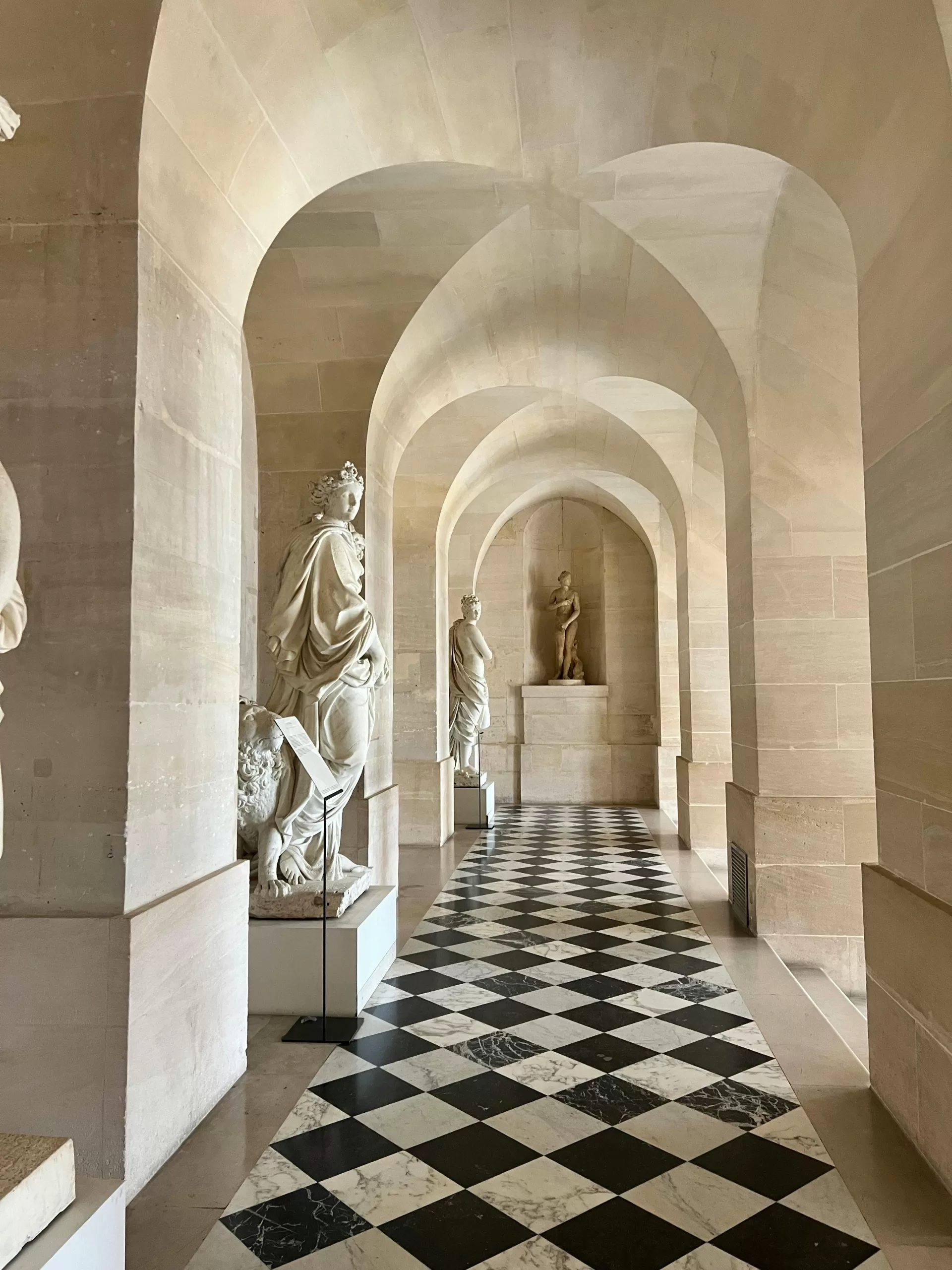 "A timeless marble hallway lined with classical statues and a checkerboard floor at a grand European palace — evoking the sophistication of old-world luxury travel.