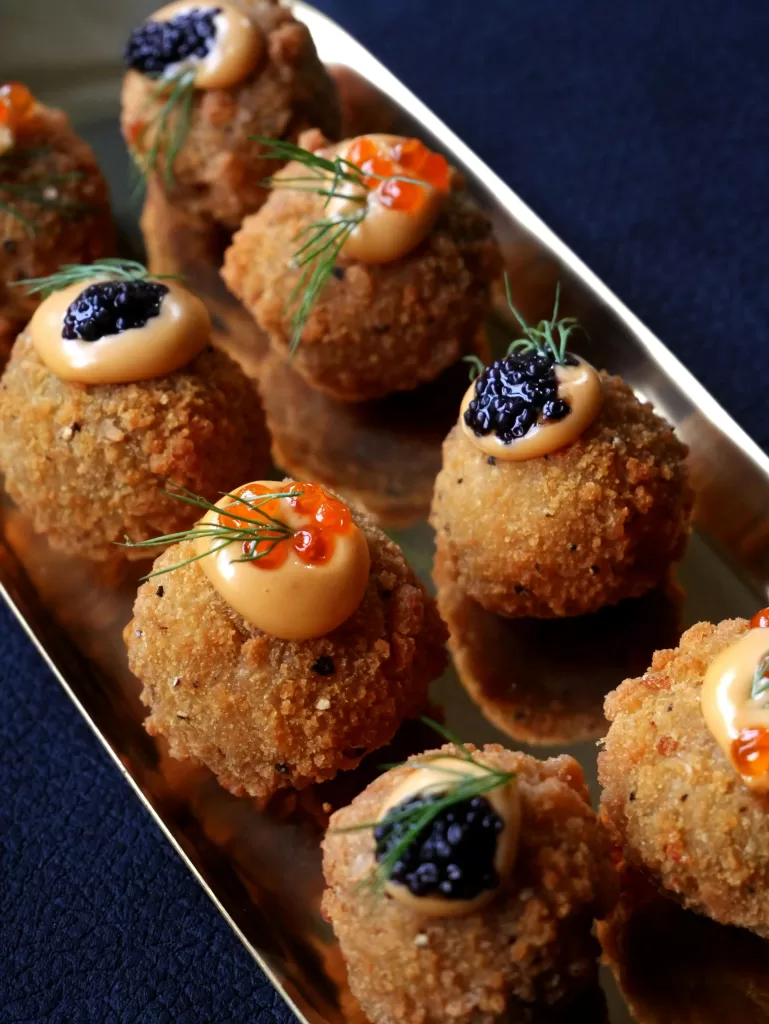 Top Private Experiences in London for Those Who Value Discretion 5 Elegant bite-sized gourmet croquettes topped with caviar, roe, and dill, served on a gold tray—perfect for upscale entertaining. | Travel Tips | Elle Blonde Luxury Lifestyle Destination Blog