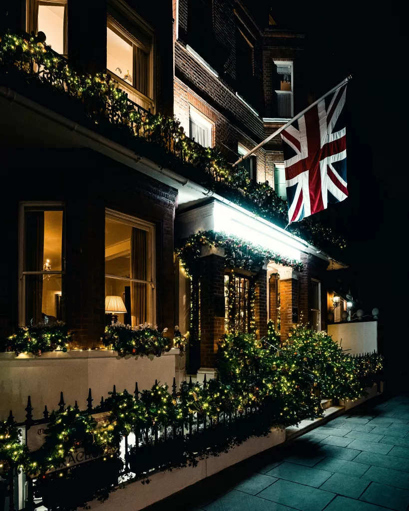 Top Private Experiences in London for Those Who Value Discretion 4 A red-brick London townhouse glowing at night, dressed in festive garlands and twinkling fairy lights beneath the Union Jack. | Travel Tips | Elle Blonde Luxury Lifestyle Destination Blog Top Private Experiences in London for Those Who Value Discretion