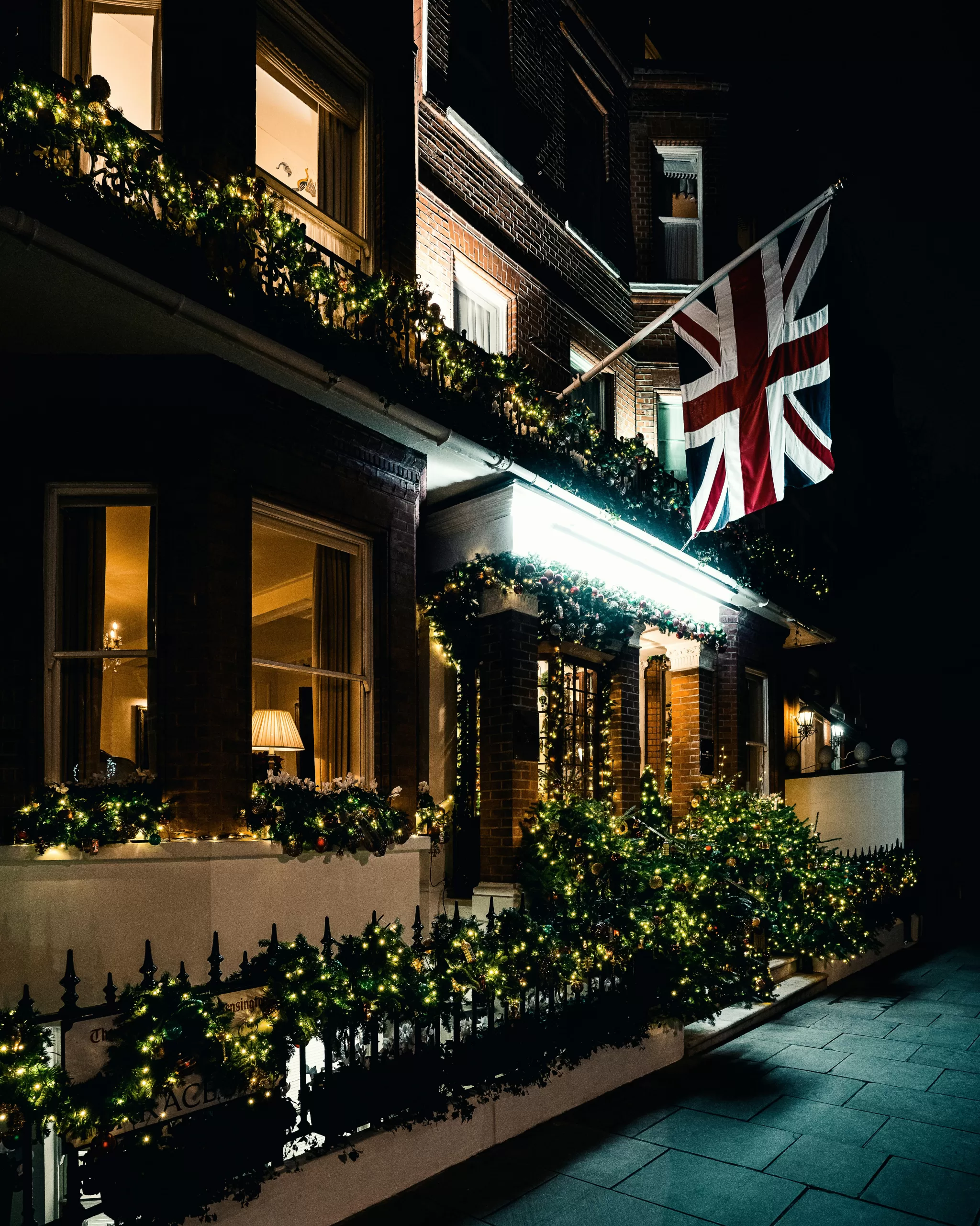 A red-brick London townhouse glowing at night, dressed in festive garlands and twinkling fairy lights beneath the Union Jack. | Travel Tips | Elle Blonde Luxury Lifestyle Destination Blog Top Private Experiences in London for Those Who Value Discretion