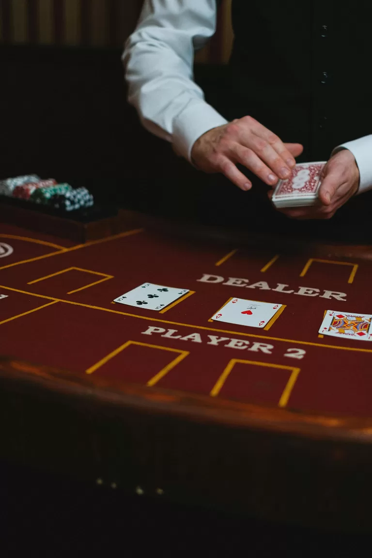 A close-up of a man’s hand elegantly holding poker chips beside a crystal glass of whisky and cigar, adorned with a sparkling diamond ring. | How to Gamble Smart and Stylishly | Elle Blonde Luxury Lifestyle Destination Blog