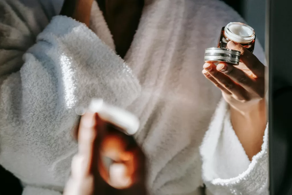 5 Restorative Techniques to Recharge After a Long Flight 2 A woman in a plush white robe applies luxury face cream in front of a mirror, indulging in a restorative skincare ritual at a five-star spa retreat. | 5 Restorative Techniques to Recharge After a Long Flight | Elle Blonde Luxury Lifestyle Destination Blog