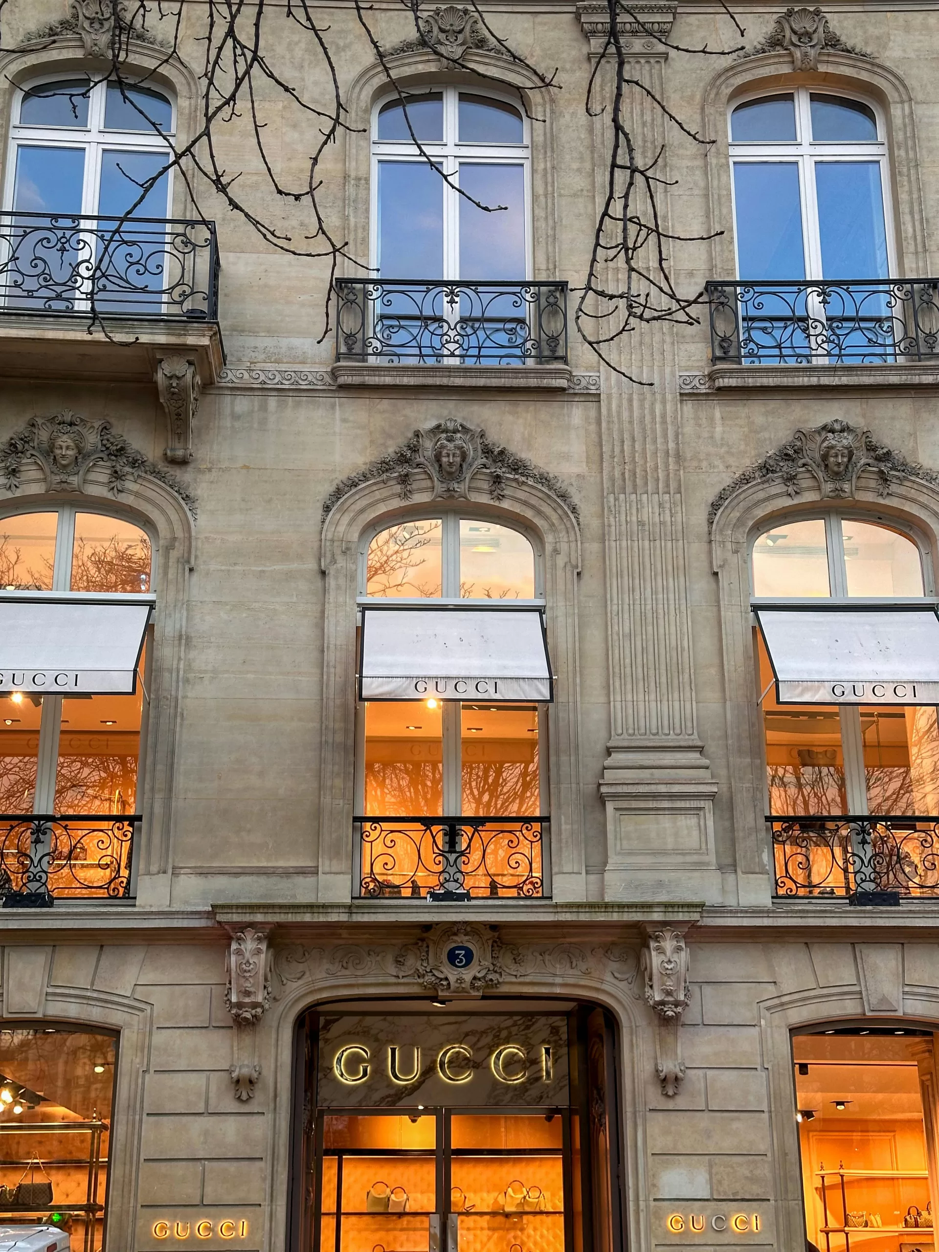 The Paris flagship of Gucci, glowing with warm light behind ornate iron balconies — where timeless fashion meets French elegance.