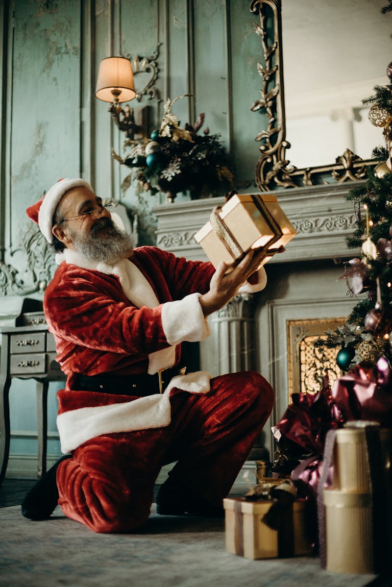 Santa Claus joyfully holding gifts by a decorated Christmas tree indoors.
