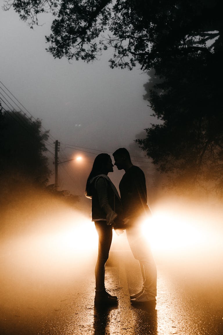 Silhouetted couple standing in front of car headlights on a foggy night, embracing romance. manifest love after heartbreak