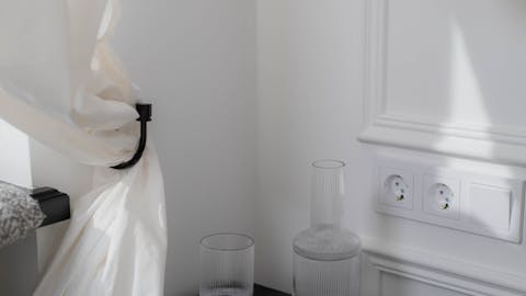 Stylish bedroom corner featuring a wooden table with glass bottles, soft white curtain, and hanging lamp.