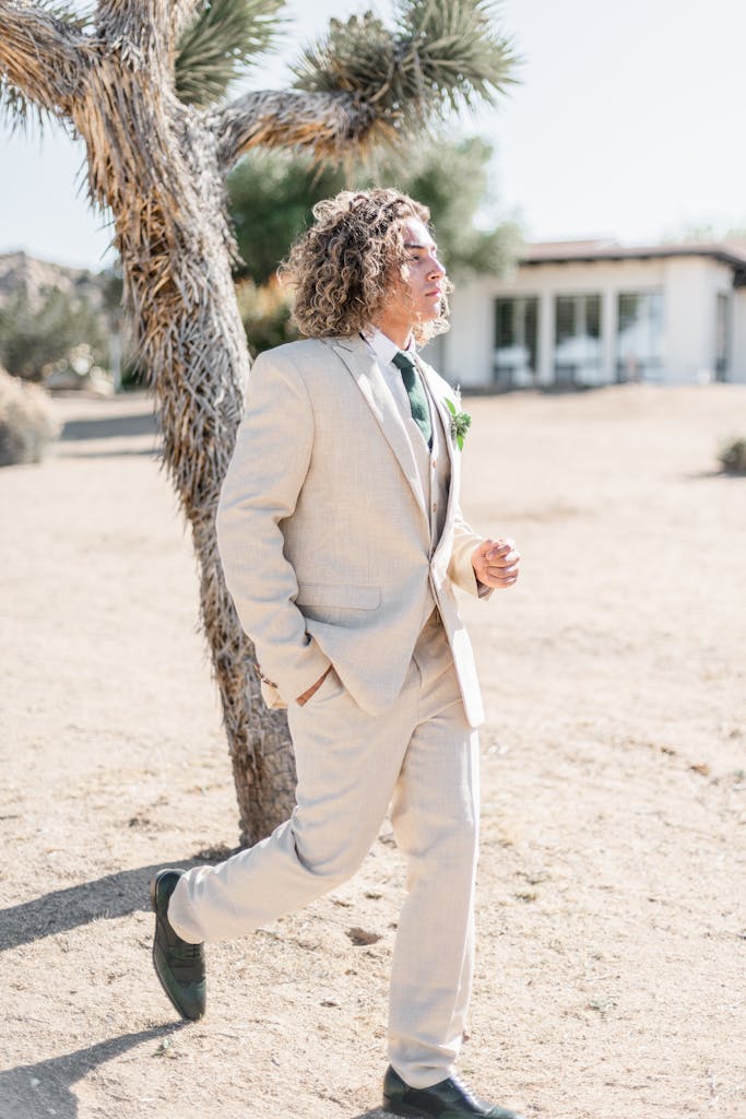 Stylish groom in suit strolling through a sunny desert landscape during a wedding.