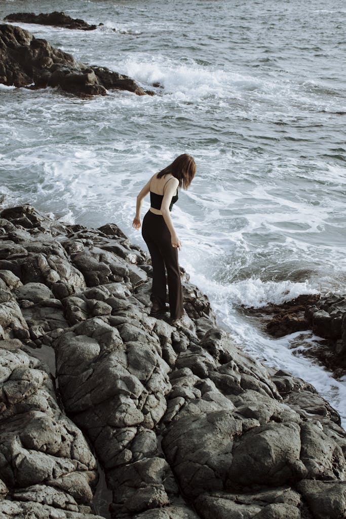 5 Ways to Reignite Self Worth After a Breakup 3 Woman exploring rocky seaside in a black outfit with ocean waves crashing nearby.
